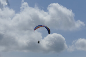 Paraglider, turning in lift with puffy cumulus behind.