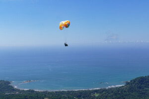 Paraglider, high in the sky with the beach in the background.