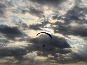 A paraglider in front of clouds with Crepuscular rays coming down from the clouds in front of the sun.