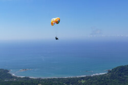 Lindsey. Loving life! Paraglider, high in the sky with the beach in the background.